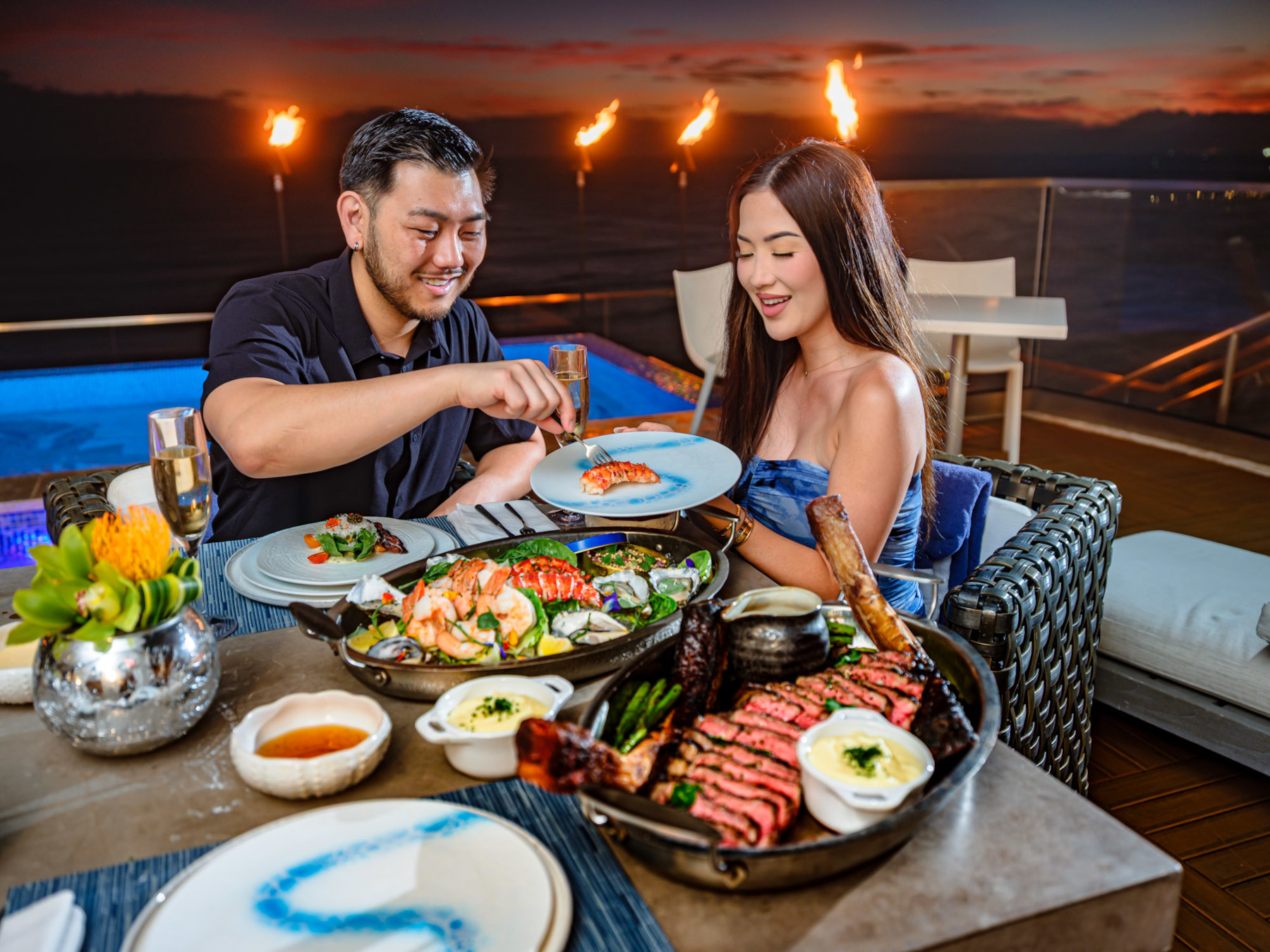 Couple enjoying dinner seafood and steak dinner with torch lights in the background